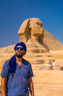 Portrait of a young tourist dressed in blue and a blue turban at the Great Sphinx of Giza. Cairo