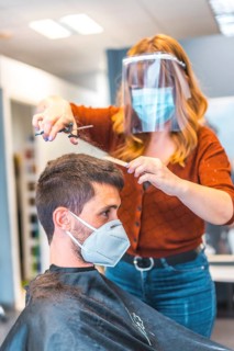 Hairdressers after the Coronavirus pandemic. Caucasian hairdresser with face mask and protective screen