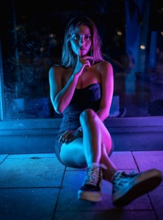 Caucasian brunette in a black dress illuminated by purple and blue led light reflected in black crystals sitting on the floor