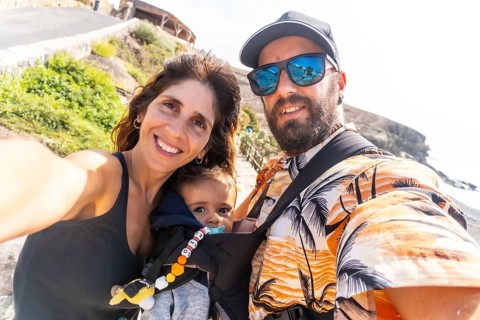 A father with his son in his backpack and the mother on vacation on the beach of Ajuy