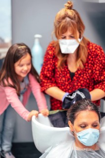 Hairdresser with mask and gloves washing the hair of the client and her daughter playing winged. Reopening with security measures for hairdressers in the Covid-19 pandemic