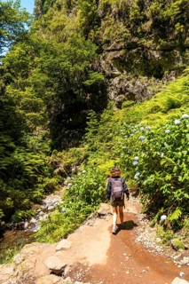A young woman on the trail next to the waterfall at Levada do Caldeirao Verde