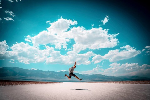 A young man jumping with a blue shirt on the white salt of Badwater Basin