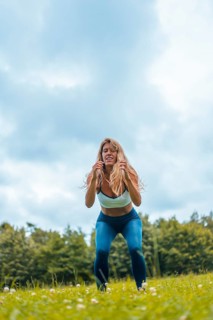 Fitness session with a young blonde caucasian woman exercising in nature with a blue maya on her feet and a white short shirt. Squatting and jumping