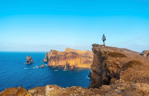 A young man on a cliff at Ponta de Sao Lourenco on the coast with rock formations in summer