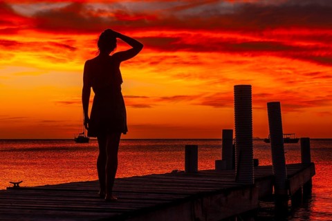 A young woman walking towards the Caribbean Sea in the orange sunset at the West End beach of Roatan. Honduras