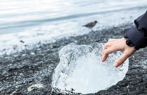 A hand stroking ice on the beach of Jokulsarlon Ice Lake in the Golden Circle of southern Iceland