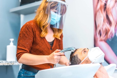 Reopening of hairdressing salons after the Coronavirus pandemic. Hairdresser with face mask and protective screen