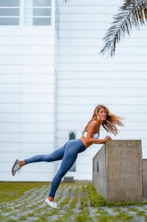 Fitness and yoga session with a young blonde Caucasian instructor dressed in a casual outfit with blue Maya and a white T-shirt. Stretching with a white wall in the background
