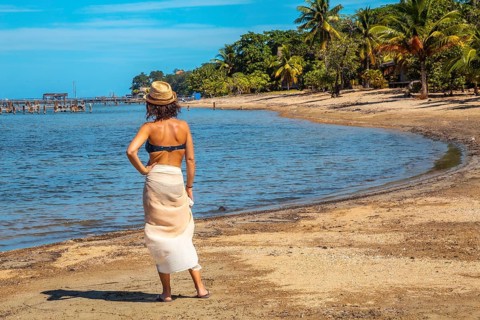 A young tourist in a bikini and skirt on the beach of Sandy Bay on Roatan Island looking at the Caribbean Sea. Honduras