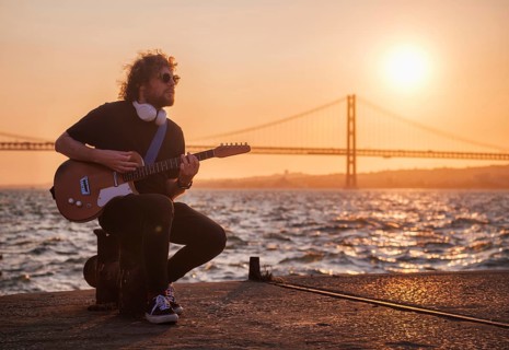 Hipster street musician in black playing electric guitar in the street on sunset