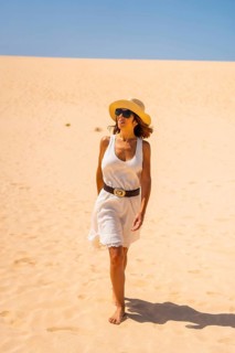 A young tourist in a white dress and a hat walking through the dunes of the Corralejo Natural Park
