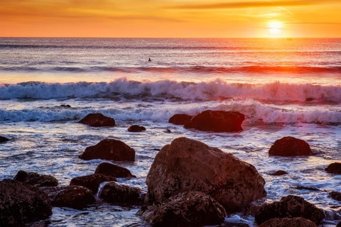 Atlantic ocean sunset with waves and rocks and surfers silhouettes in water at Costa da Caparica
