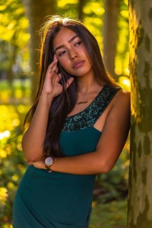 A young brunette Latina with long straight hair leaning against a tree in a green dress. Portrait with a sweet and sensual look
