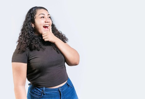 Happy young woman holding chin looking at an advertisement to side. Excited latin woman with hand on chin looking a promo to the side isolated