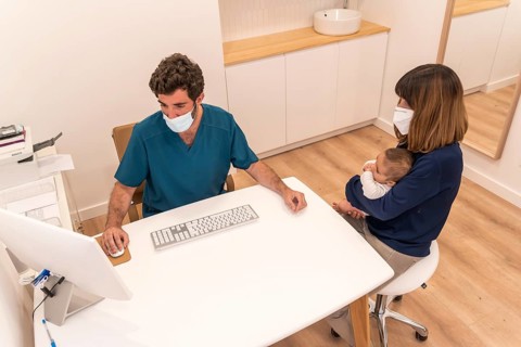 High angle view of a woman with baby in arms in a pediatric appointment sitting and talking with a doctor