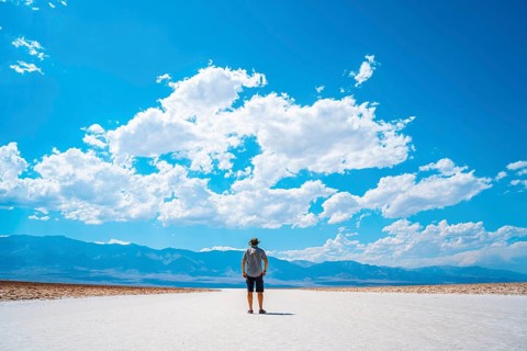 A young man jumping with a blue shirt on the white salt of Badwater Basin