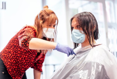 Hairdresser with mask and gloves cutting the ends with scissors to the client. Reopening with security measures for hairdressers in the Covid-19 pandemic