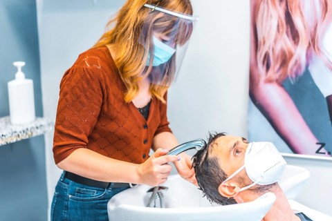 Reopening of hairdressing salons after the Coronavirus pandemic. Hairdresser with face mask and protective screen