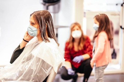 Hairdresser with mask and gloves talking to the client's daughter while the client answers an important call. Reopening with security measures for hairdressers in the Covid-19 pandemic