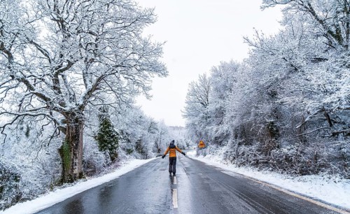 A young woman in a yellow jacket walking along an icy road and denied trees. Snow in the town of Opakua near Vitoria in Araba
