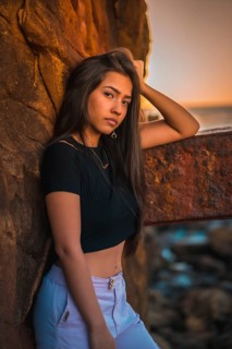 A young pretty brunette Latina with long straight hair in a short black T-shirt and pink pants. Portrait of the woman leaning on a sculpture with scab