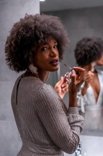 A young black girl with afro hair putting on makeup before the party with a smile. Exclusive party
