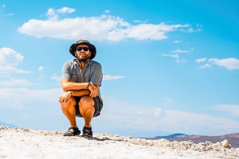 A young man crouched on his back on the white salt flat in Badwater Basin