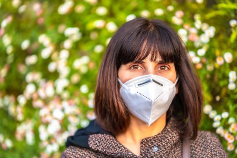 Portrait of a young woman with a mask next to a beautiful daisies. First walks of the uncontrolled Covid-19 pandemic