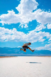 A young man jumping with a blue shirt on the white salt of Badwater Basin