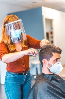 Hairdressers after the Coronavirus pandemic. Hairdresser with face mask and protective screen