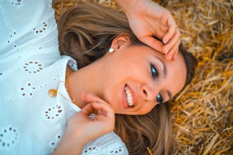 A young blonde Caucasian woman in a white dress in a field of dry straw atop a haystack