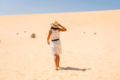 Tourist in white dress and hat walking through the dunes of the Corralejo Natural Park
