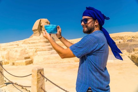 A young man putting on the mask facing the Great Sphinx of Giza and the Pyramids of Giza in the background