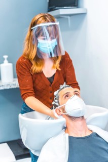 Hairdressers after the Coronavirus pandemic. Caucasian hairdresser with face mask and protective screen