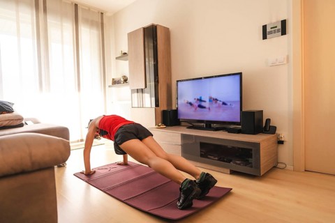 A young woman doing push-ups in the room watching TV. Sport in the covid19 quarantine at home