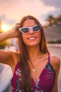 Portrait at sunset with a brunette in a maroon floral dress and white sunglasses enjoying the summer in the golden hour