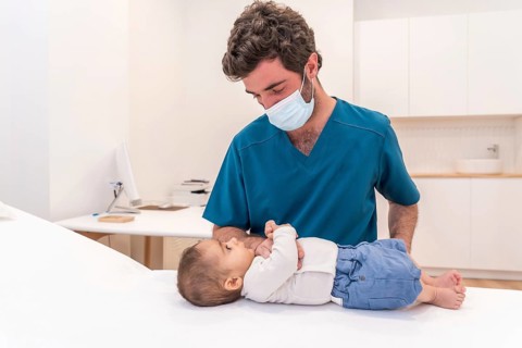 Adorable newborn baby lying on stretcher while getting examined by a doctor during his checkup