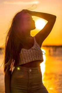 Summer lifestyle. A young blonde Caucasian woman in a white short wool sweater on a beach sunset. Thinking and looking at the sea
