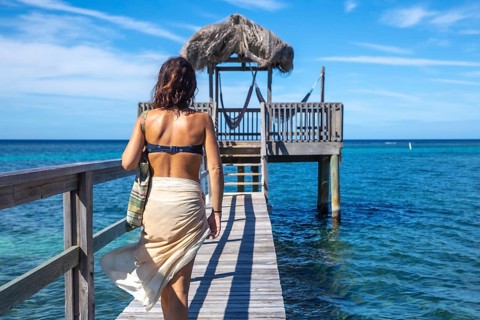 A young girl in a bikini walking to a wooden construction of the Caribbean Sea on Roatan Island. Honduras