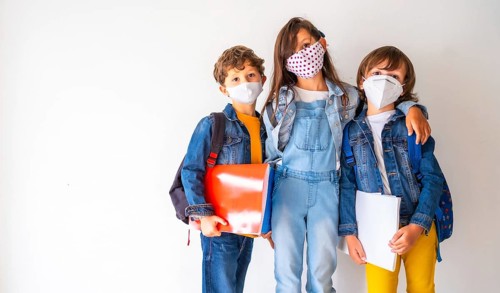 Three children with face masks ready to go back to school. New normality