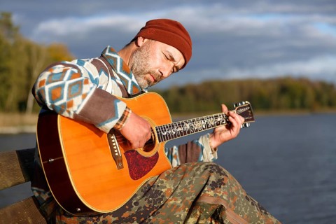 Man playing guitar on a jetty by the lake