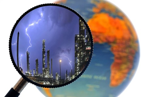 Lightning during thunderstorm above petrochemical industry seen through magnifying glass held against illuminated terrestrial globe