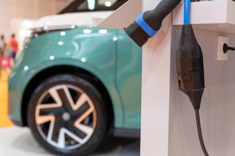 EV charger and a blue electro car parked at the background. Mid shot