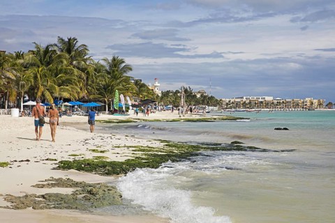 Western tourists walking on white sandy beach and hotels along Playa Del Carmen