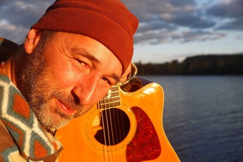 Man playing guitar on a jetty by the lake