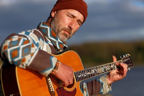 Man playing guitar on a jetty by the lake