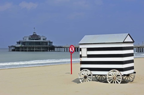 Striped beach cabin on wheels and seaside pier of Blankenberge