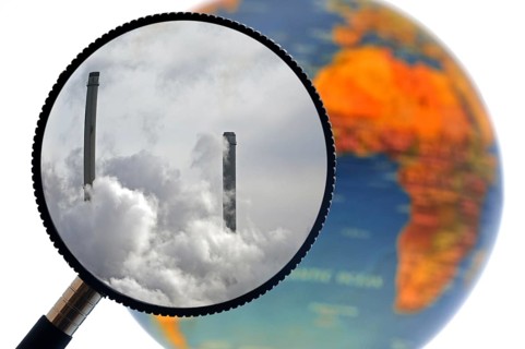 Chimneys covered in smoke seen through magnifying glass held against illuminated terrestrial globe