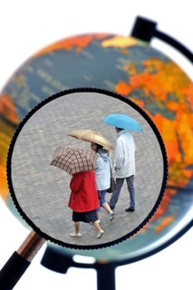 Tourists walking in the rain with umbrellas in summer seen through magnifying glass held against illuminated terrestrial globe